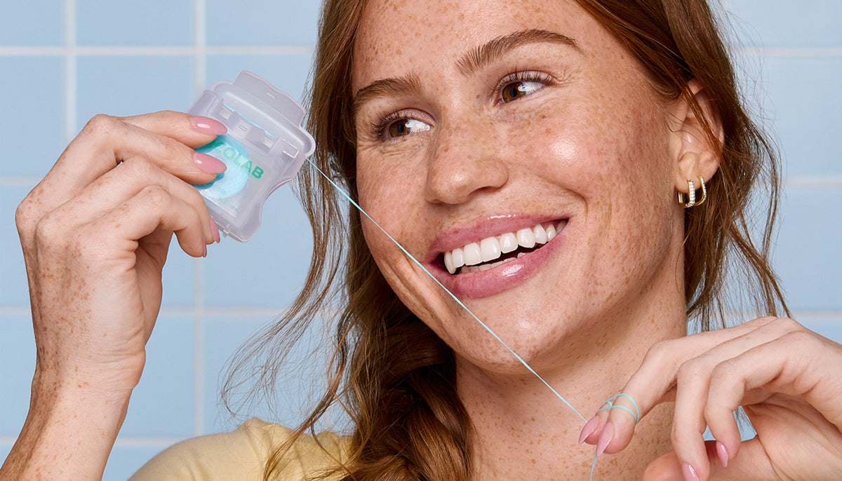 Woman using a clear dental tool against a tiled bathroom wall.