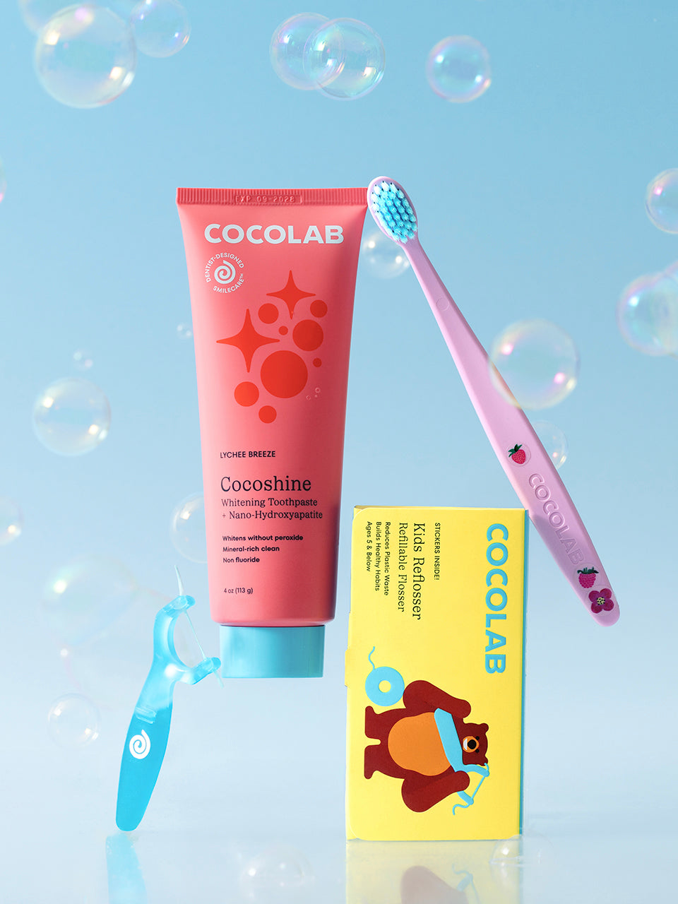 Cocolab skincare products including a pink tube, yellow box, and pink toothbrush on a light blue background with bubbles.