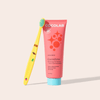 Pink toothpaste tube with colorful brush on a light beige background