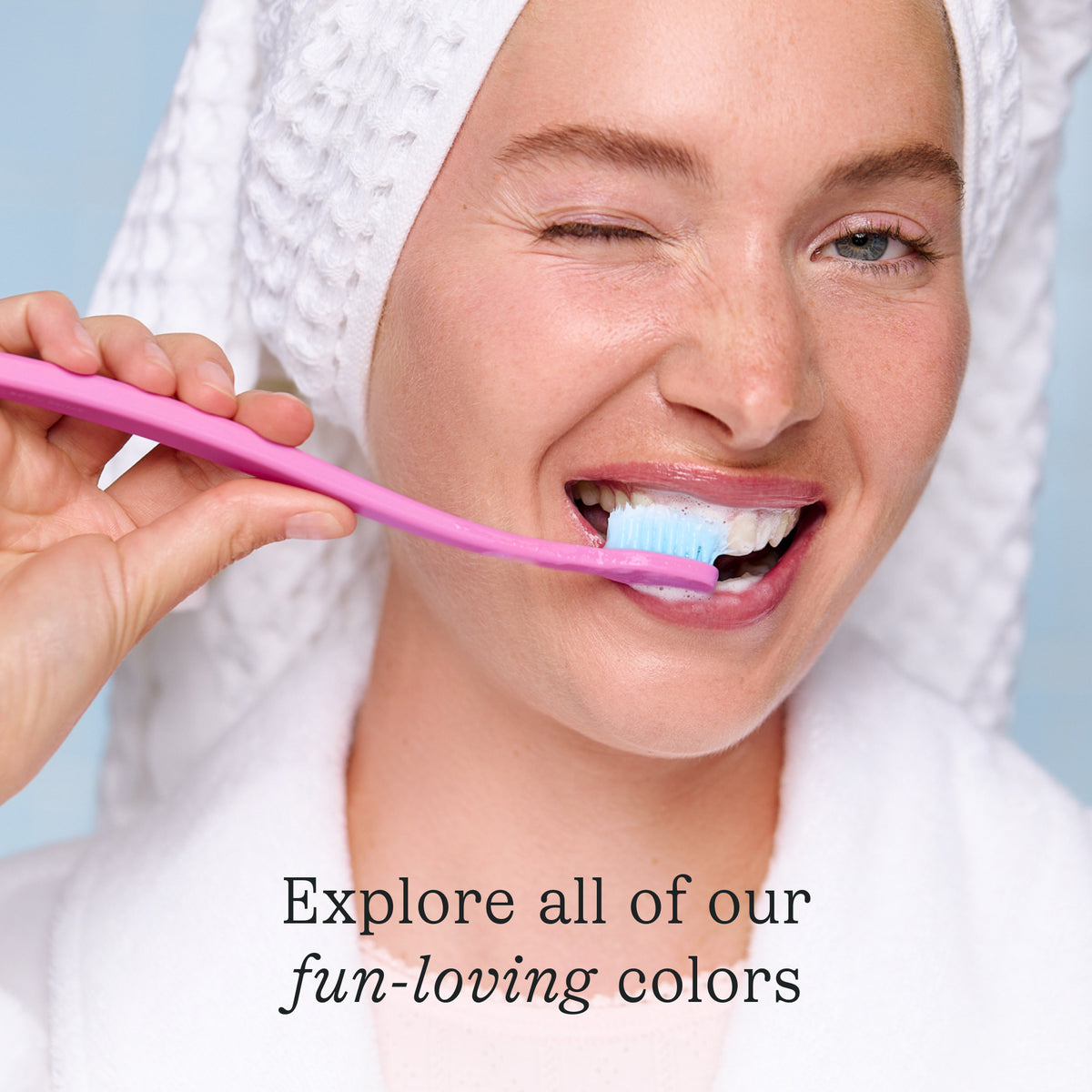 Woman brushing her teeth with a pink toothbrush against a light blue background