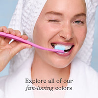 Woman brushing her teeth with a pink toothbrush against a light blue background