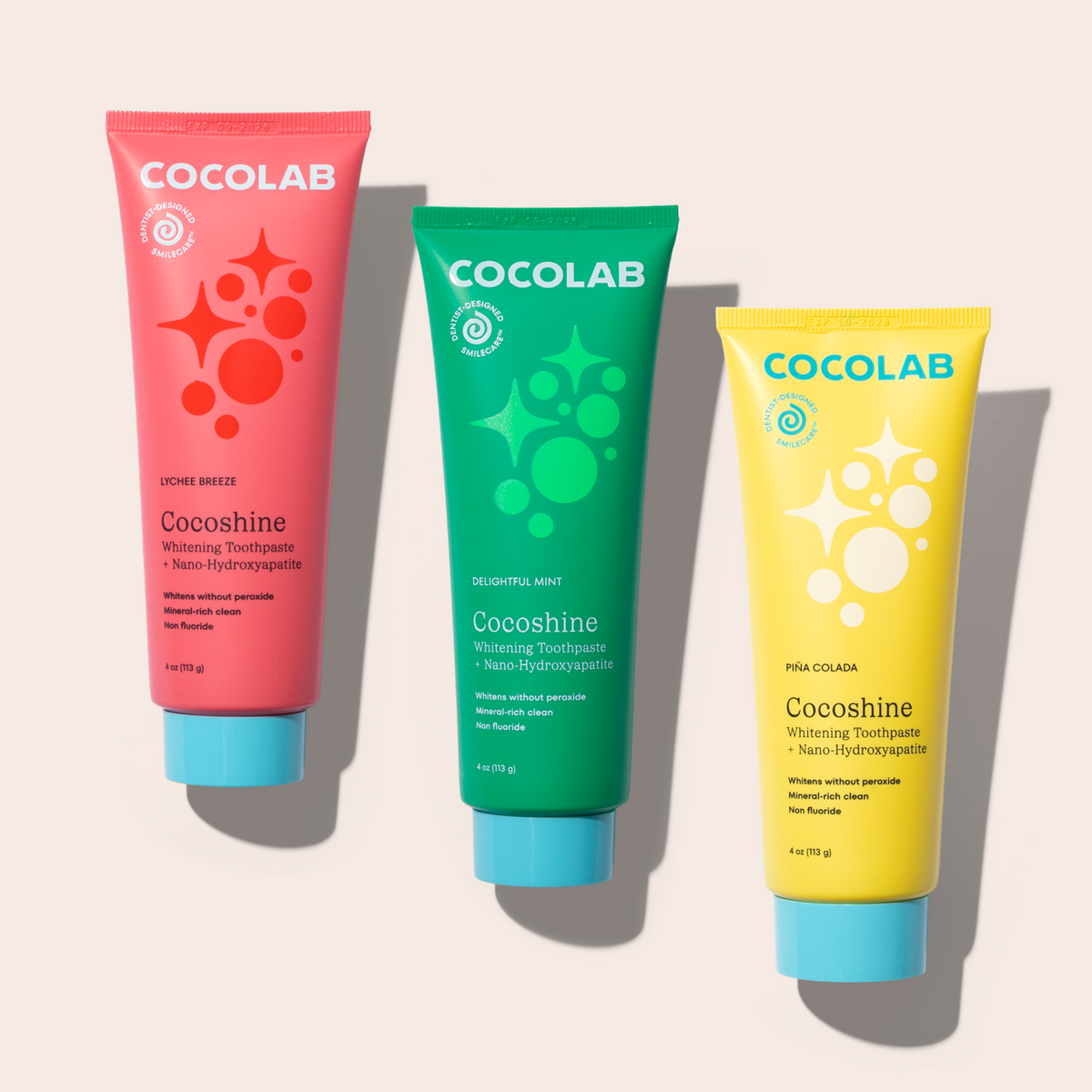 Three Cocolab toothpaste tubes in pink, green, and yellow on a light gray background