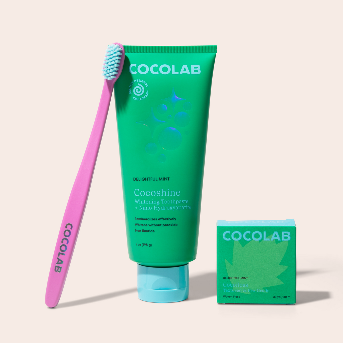 Cocolab toothpaste tube, toothbrush, and cocofloss on a beige background