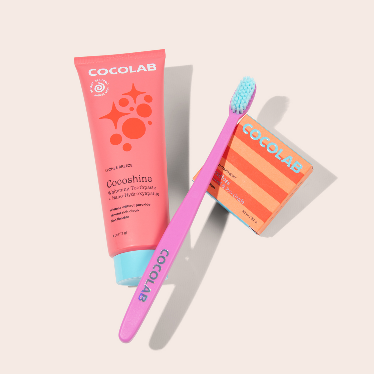 Cocoshine toothpaste tube, pink toothbrush, and Cocolab packaging on a light beige background