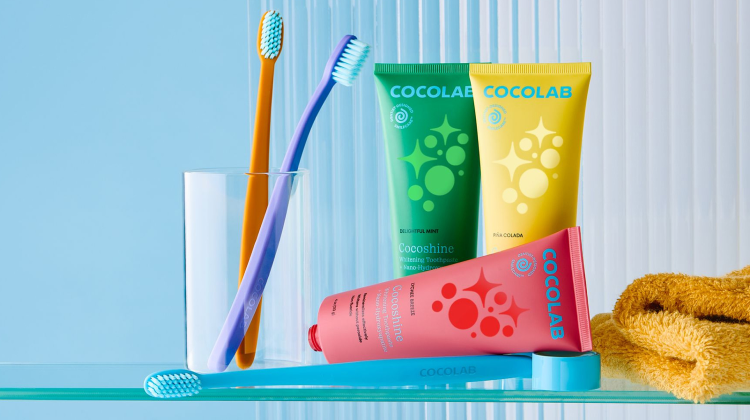 Cocolab toothpaste, toothbrushes, and a towel on a glass shelf with a blue background