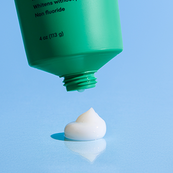 Green toothpaste tube with a small amount of white toothpaste on a blue background