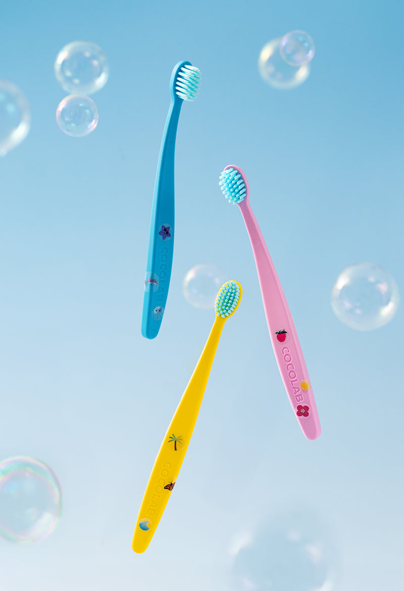 Three colorful toothbrushes with cartoon designs on a blue background with bubbles.