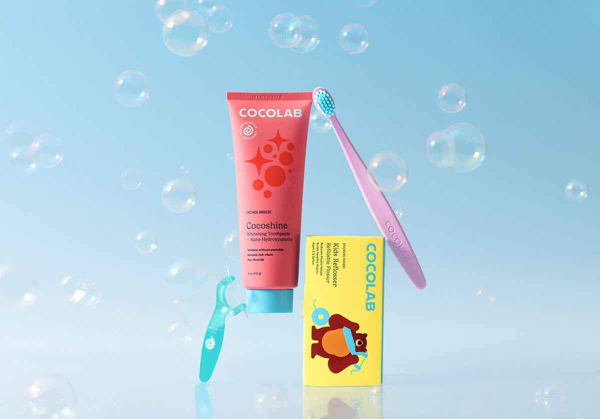 Cocolab children's toothpaste, toothbrush, and mouthwash on a light blue background with bubbles.
