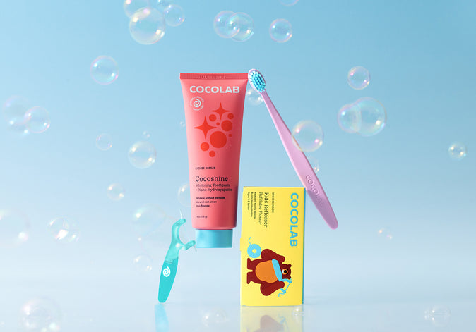 Cocolab children's toothpaste, toothbrush, and mouthwash on a light blue background with bubbles.