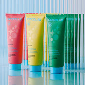 Colorful Cocolab Cocoshine on a reflective surface with a striped background