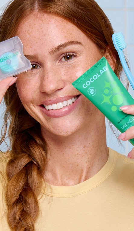 Woman holding cocoshine and cocofloss with a blue toothbrush in the background