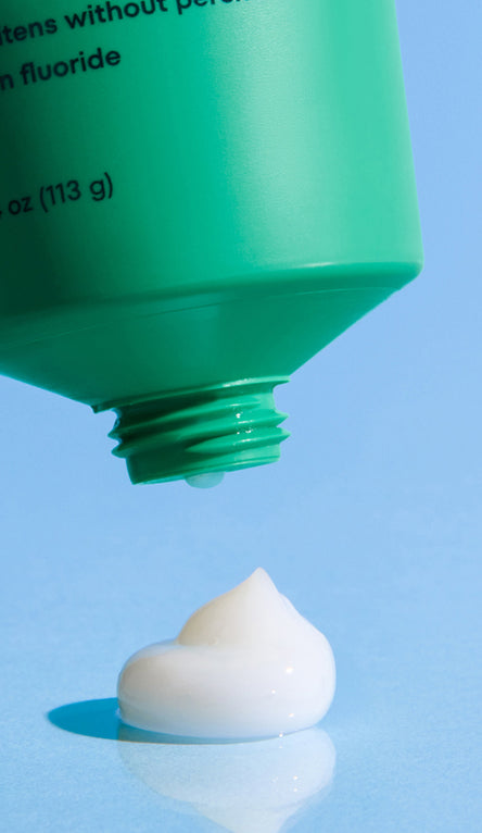 Green tube of toothpaste with a white paste on a blue background