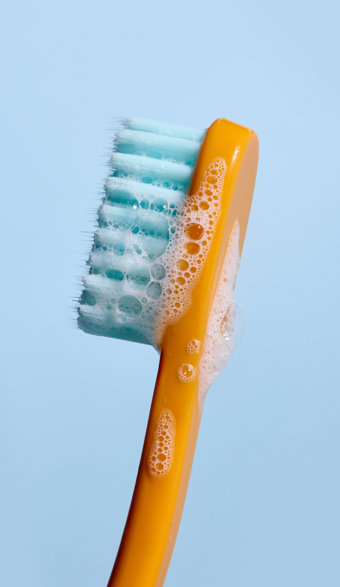 Orange toothbrush with blue bristles and foam on a light blue background