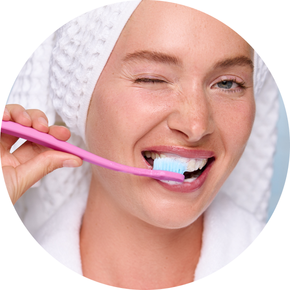 Woman brushing her teeth with a pink toothbrush in a close-up shot.
