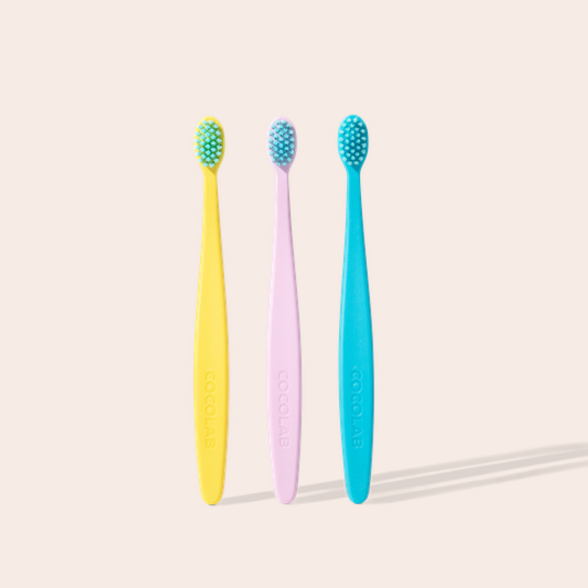 Three colorful toothbrushes on a light beige background
