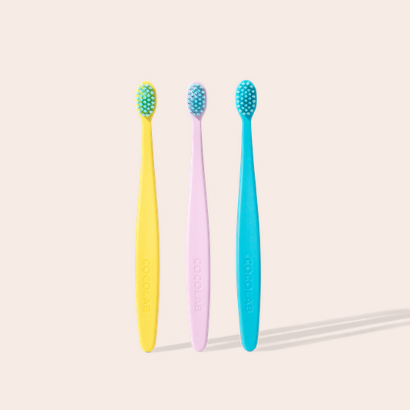Three colorful toothbrushes on a light beige background