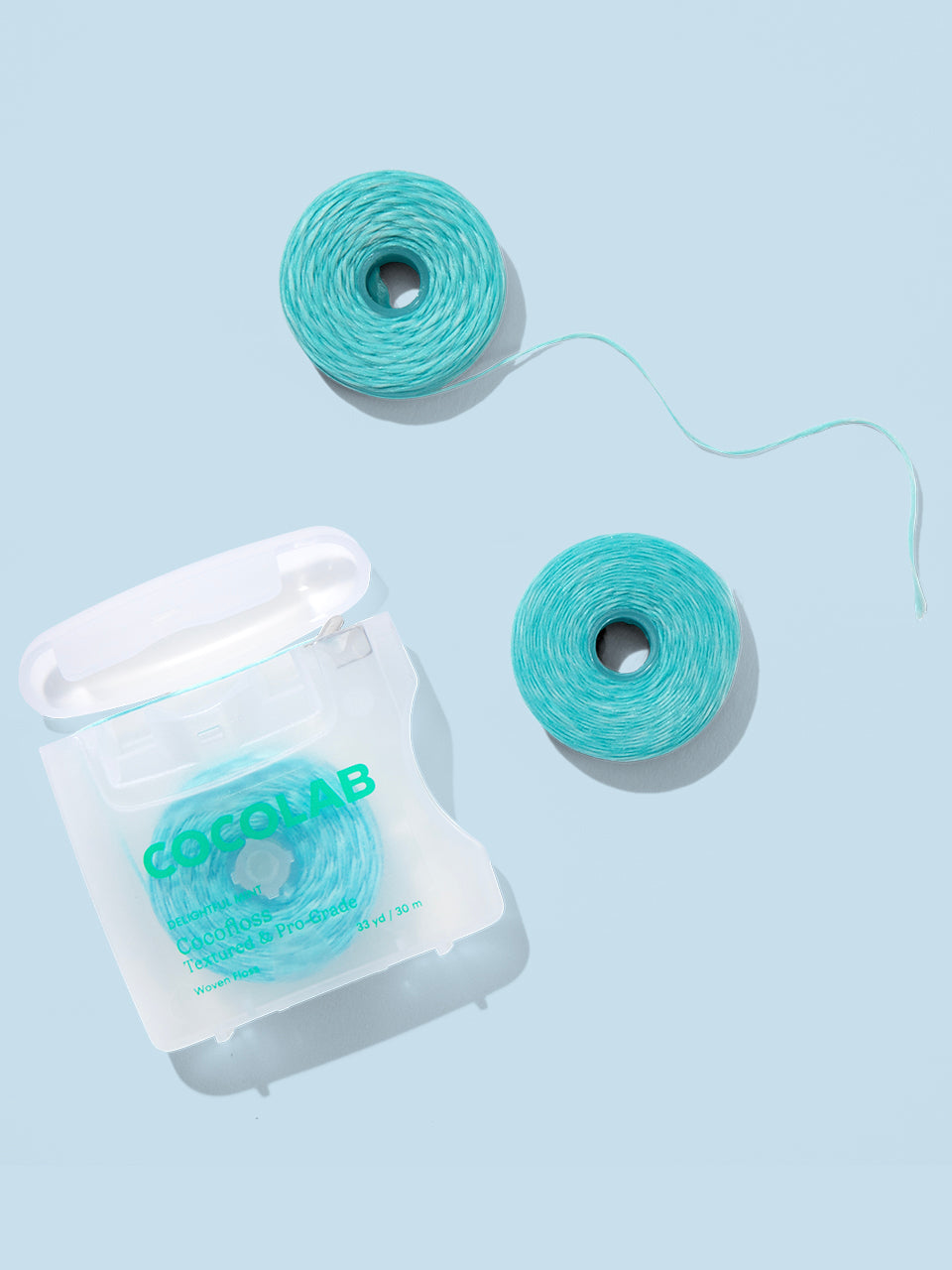 Two spools of cocofloss thread and a clear container with a brand logo on a light blue background