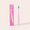 Pink toothbrush with blue bristles next to its packaging on a light pink background